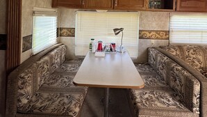Ein kompaktes Wohnmobil-Interieur mit Esstisch, zwei gepolsterten Sitzbereichen, Holzschränken und einem Dachlüfter.