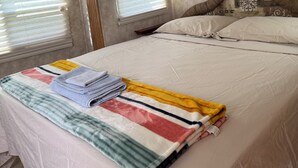 Ein Schlafzimmer mit einem Bett, einem Fenster mit Jalousien, einem Kopfteil und einer Wandleuchte.