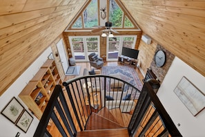 Ein geräumiges Loft mit Holzvertäfelung, einer Treppe, einer Sitzecke mit Fernseher und großen Fenstern mit Blick ins Freie.