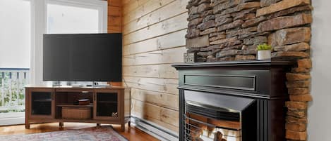 Ein Wohnzimmer mit Kamin aus Stein, einem Fernseher auf einem Holzschrank und einer großen Uhr an der Wand.