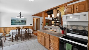 A kitchen with wooden cabinets, a dining table, chairs, a stove, and a chandelier. - Blue Ridge Retreat w/ Private Trail (Pisgah Forest)
