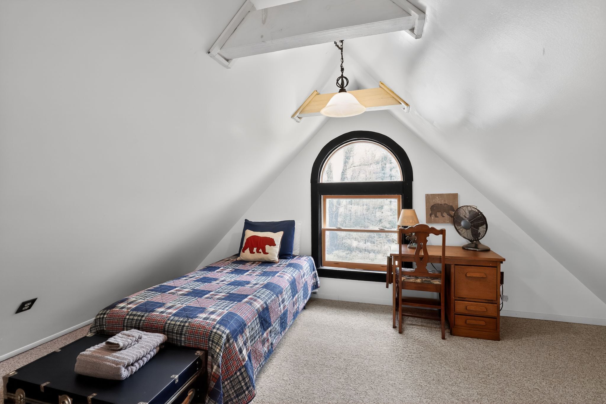A bedroom with a bed, a desk, a chair, a window, and a ceiling fan.