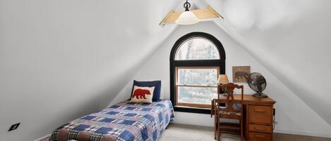 A bedroom with a bed, a desk, a chair, a window, and a ceiling fan.