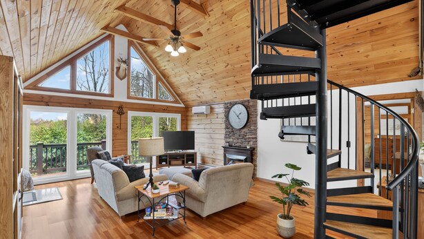 A spacious living area with a fireplace, a sofa, a television, and a large window overlooking greenery. - Blue Ridge Retreat w/ Private Trail (Pisgah Forest)