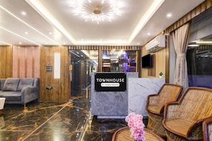 A reception area with a marble floor, a reception desk labeled 'TOWNHOUSE,' a grey sofa, wicker chairs, and a modern chandelier.