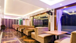 A hotel room with a marble floor, beige seating, a large window with curtains, and a ceiling with recessed lighting.