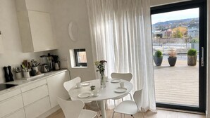 Moderni keittiö, jossa on valkoiset kaapit, ruokapöytä tuoleineen ja suuri ikkuna, josta avautuu näkymä kaupunkiin.