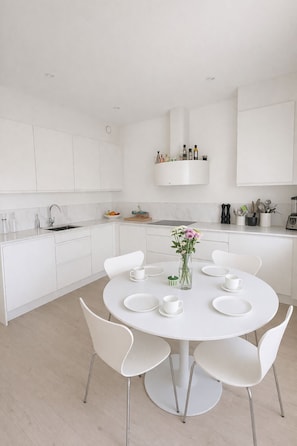 Een moderne keuken met witte kastjes, een ronde eettafel met stoelen, en een bloemenvaas op de tafel.