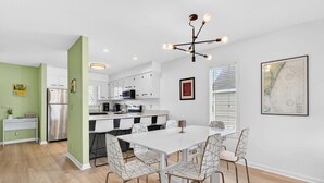 Una cocina moderna con armarios blancos, un refrigerador de acero inoxidable y un comedor con mesa blanca y sillas de estructura metálica.