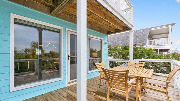 Una terraza techada al aire libre con una mesa y sillas de madera, ventanas amplias y vistas del entorno.