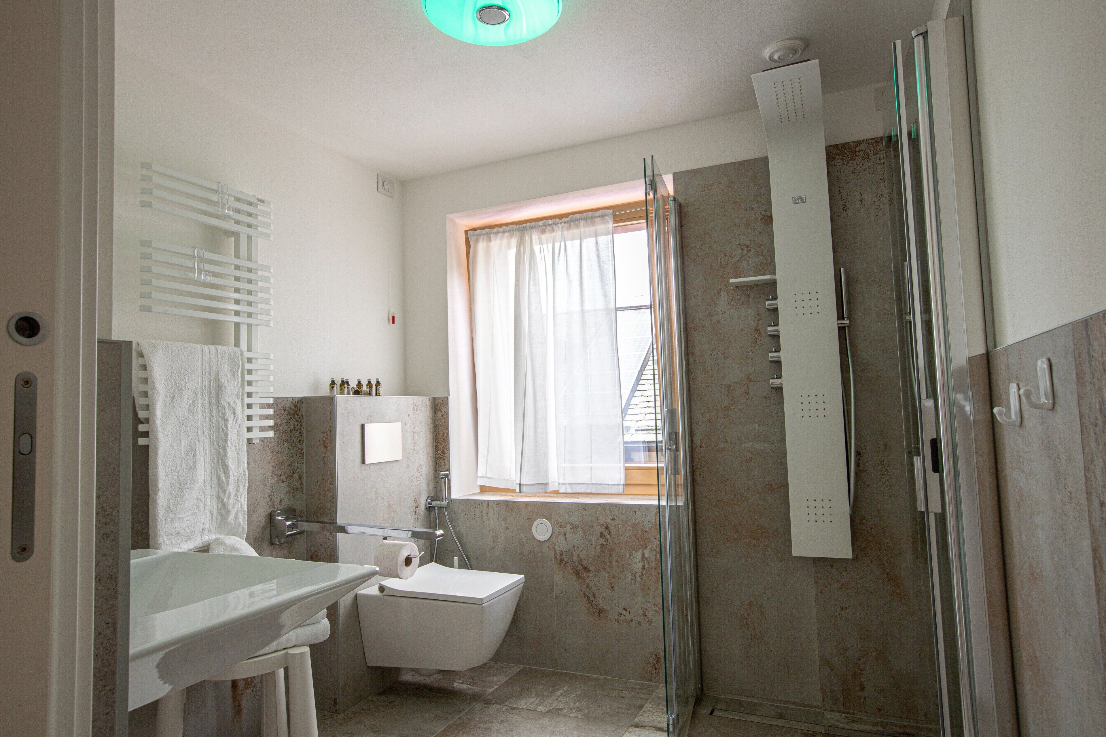 Une salle de bain équipée de toilettes, d’un lavabo, d’une douche et d’une fenêtre avec des rideaux.
