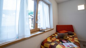 A bedroom with a bed, a window with curtains, a laptop, and a remote control on a shelf. - Chalet 'Apartment 1' with Mountain View, Shared Garden and Wi-Fi (Livigno)