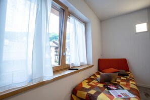 Ein Schlafzimmer mit einem Bett, einem Fenster mit Vorhängen, einem Laptop und einer Fernbedienung auf einem Regal.