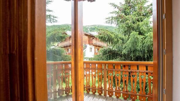 A wooden balcony with a railing, a view of a building surrounded by trees. - Chalet 'Apartment 1' with Mountain View, Shared Garden and Wi-Fi (Livigno)