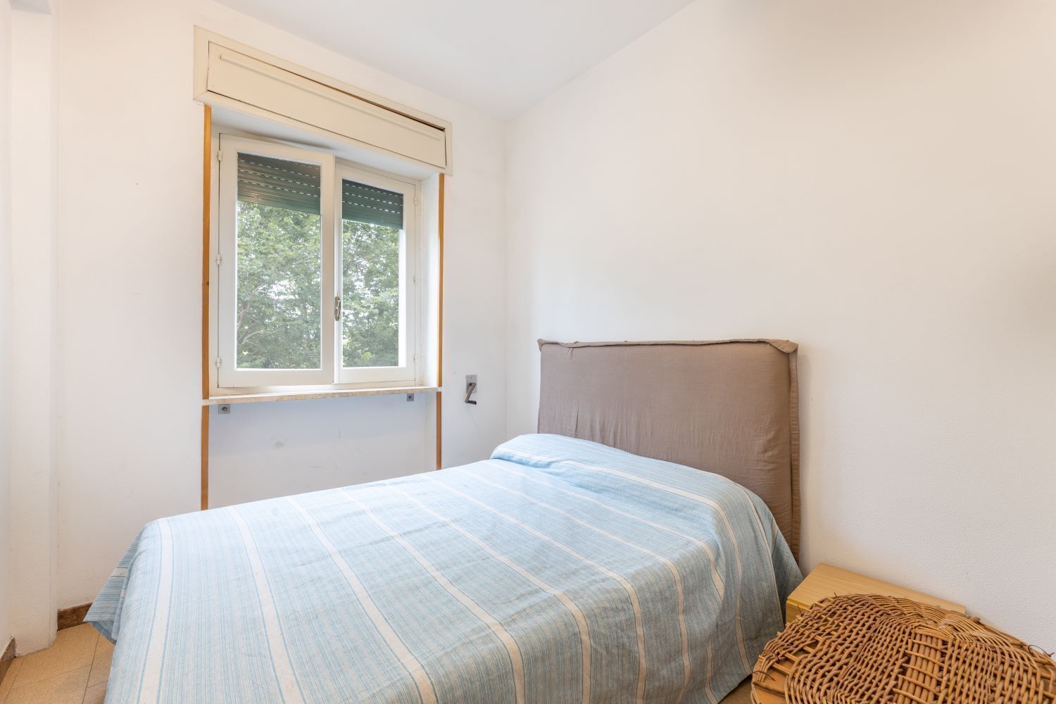 Une chambre à coucher avec un lit, une fenêtre et un panier en osier.
