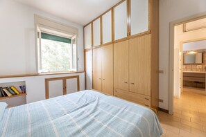 Ein Schlafzimmer mit Bett, Holzschrank, Fenster mit Jalousien und Bücherregal.