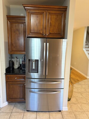 Un refrigerador de acero inoxidable con cajón congelador, dispensador de hielo incorporado y dispensador de agua.