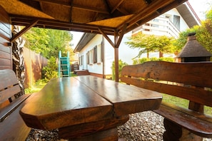 An outdoor wooden table and benches under a covered area with a view of a house and trees. - 2-room Apartment for 4 People, Rowy (Ustka)