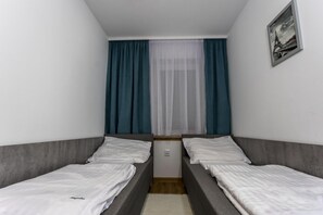 A small, narrow room with two single beds, a window with sheer curtains, and a framed picture on the wall. - 2-room Apartment for 4 People, Rowy (Ustka)