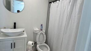 Ein Badezimmer mit rundem Spiegel, Waschbecken, Toilette und Duschvorhang.