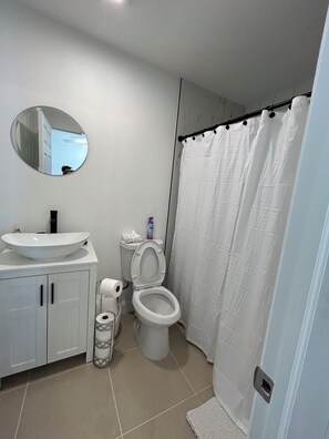 A bathroom with a round mirror, a sink, a toilet, and a shower curtain. - Delightful 1-bedroom apartment with AC in vibrant Wellington (Wellington)