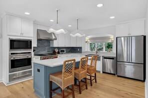 A modern kitchen with white cabinets, stainless steel appliances, a central island with bar stools, and pendant lighting. - Award-Winning Resort Amenities | Fairway Oaks 8 by Wild Dunes (Isle Of Palms)
