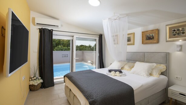 A bedroom with a bed, a TV, a window with curtains, a bedside table, and a view of a pool. - Casa Crystal Istria (Peroj)