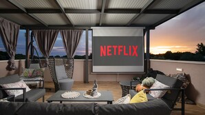 A rooftop terrace with outdoor seating, a large screen displaying 'NETFLIX,' and a sunset view. - Casa Crystal Istria (Peroj)
