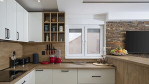 A modern kitchen with white cabinetry, a built-in stove, a fruit bowl, and a stone wall. - Casa Crystal Istria (Peroj)