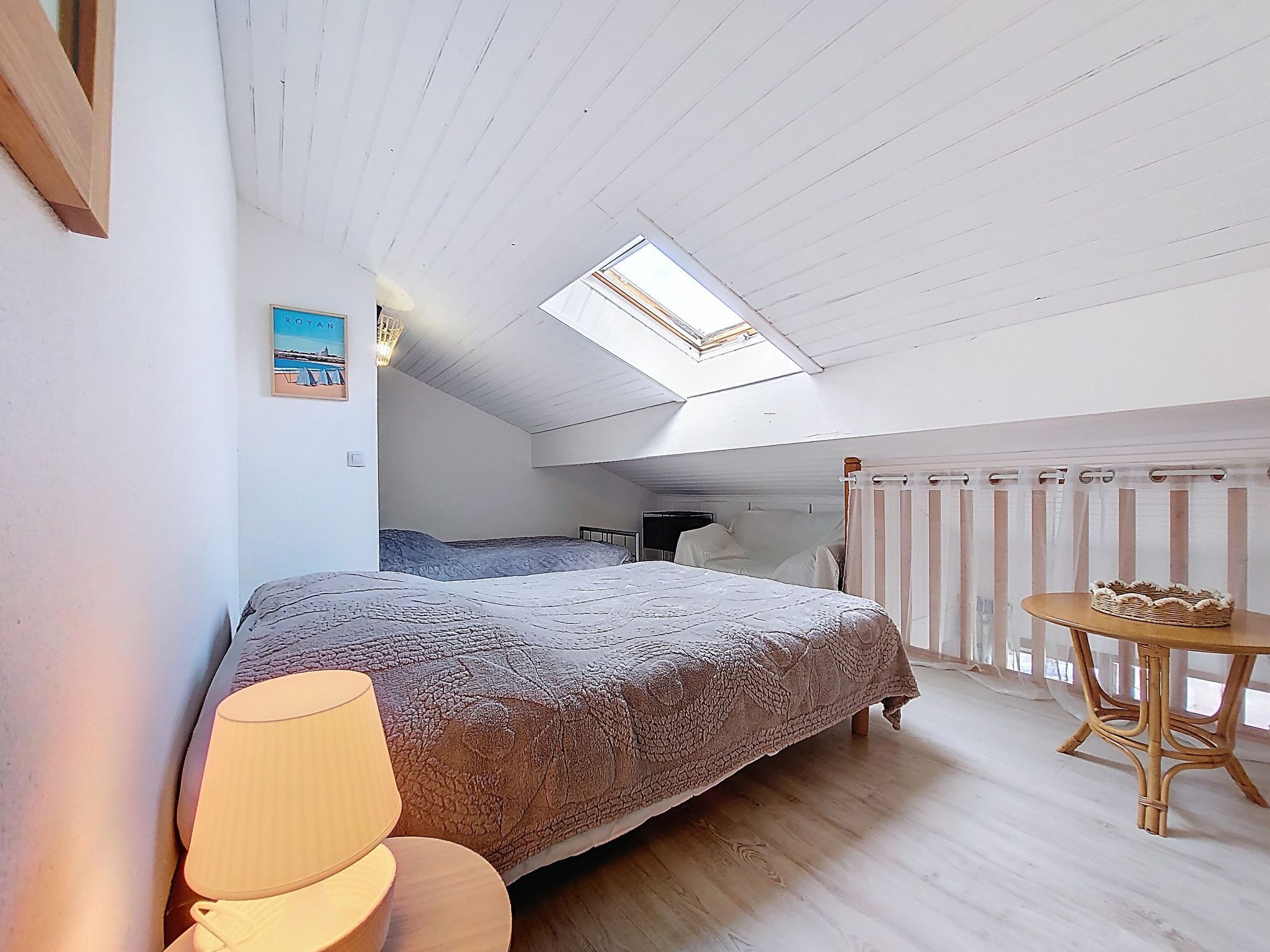 A bedroom with a skylight, a bed, a bedside table, a lamp, and a wicker chair.
