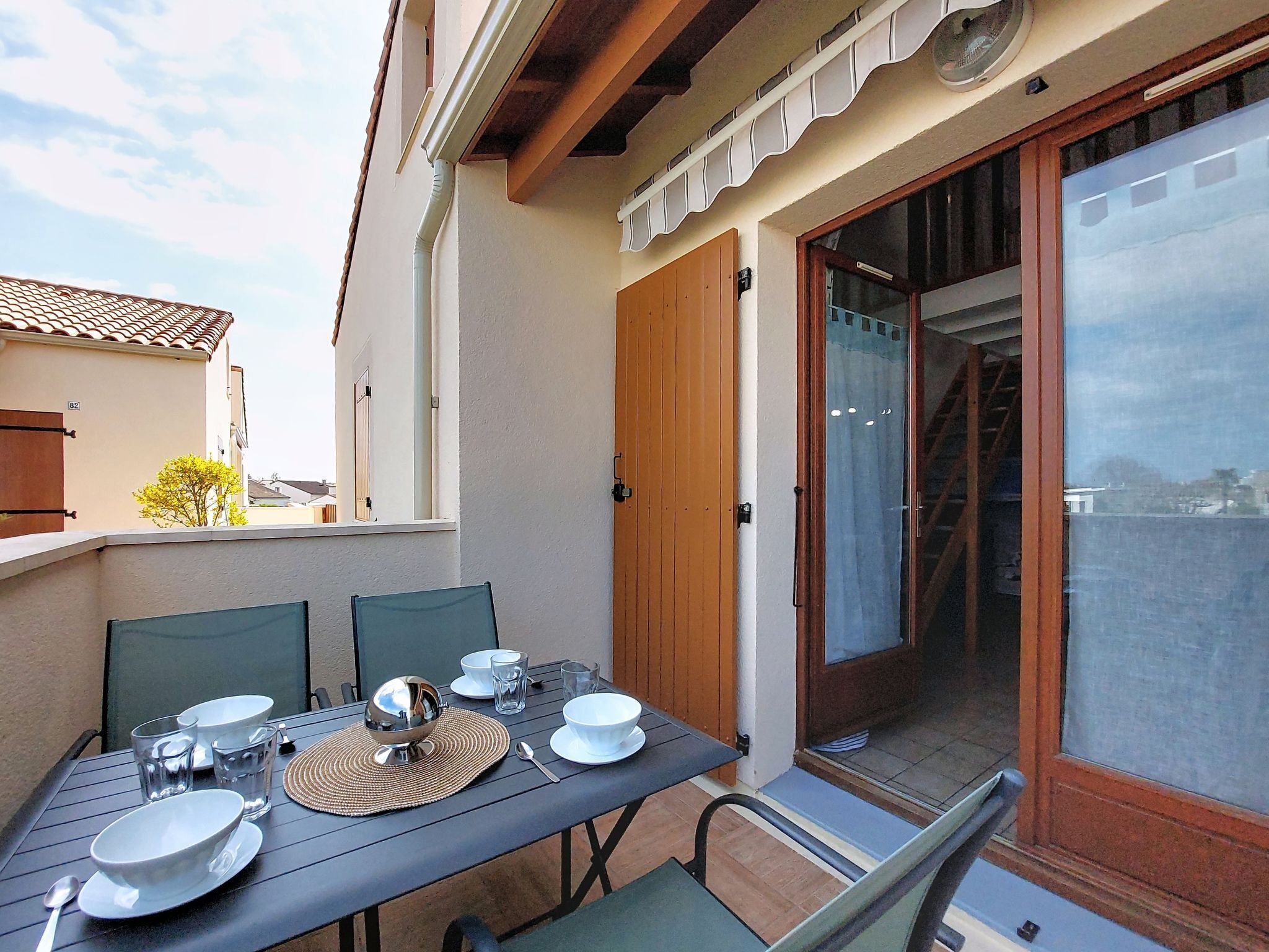 Un área de comedor al aire libre con una mesa preparada para cuatro, sillas y un ventanal corredero que da a un balcón.