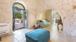 Une pièce aux murs de pierre, avec un canapé, un pouf bleu et une cheminée.