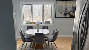 A modern kitchen with a round dining table, grey chairs, a stainless steel refrigerator, and a large window with multiple license plates. - Peaceful 4-bedroom house in charming Castine perfect for relaxing stays (Castine)