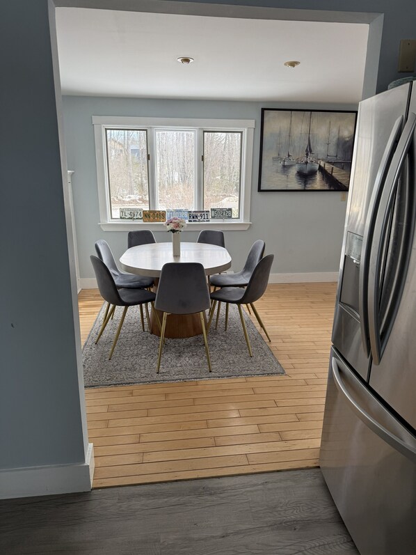 A modern kitchen with a round dining table, grey chairs, a stainless steel refrigerator, and a large window with multiple license plates.