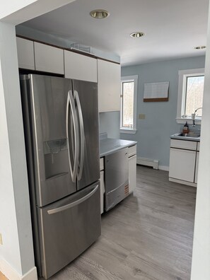 A kitchen with a stainless steel refrigerator, white cabinets, a window, and a sink.