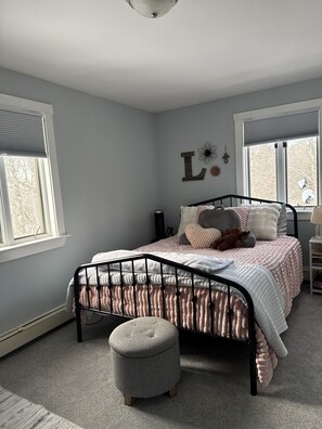 A bedroom with a bed, a bedside table, a lamp, a window, and a wall decoration.