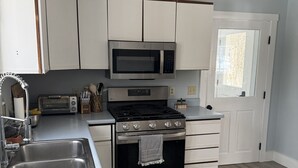 A kitchen with white cabinets, a microwave, a toaster, and a stove. - Peaceful 4-bedroom house in charming Castine perfect for relaxing stays (Castine)
