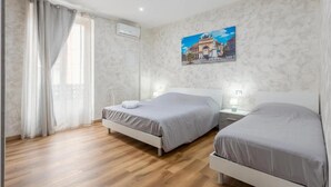 A bedroom with two beds, a window with curtains, an air conditioning unit, and a wall-mounted painting. - 'Oreto Central Station' Apartment with Balcony, Wi-Fi and Air Conditioning (Palermo)