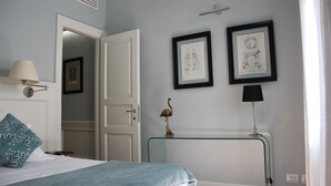Un dormitorio con una cama, una lámpara de noche, una mesita de vidrio con una lámpara, y dos cuadros en la pared.