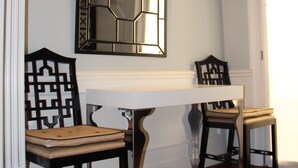 Un área de comedor con una mesa blanca, dos sillas y un espejo decorativo en la pared.