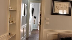 Un pasillo con una puerta que da a un baño, un cuadro en la pared y un sofá con un cojín.
