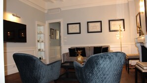 Una sala de estar con un sofá, dos sillones, un televisor de pantalla plana, obras de arte enmarcadas y una araña.