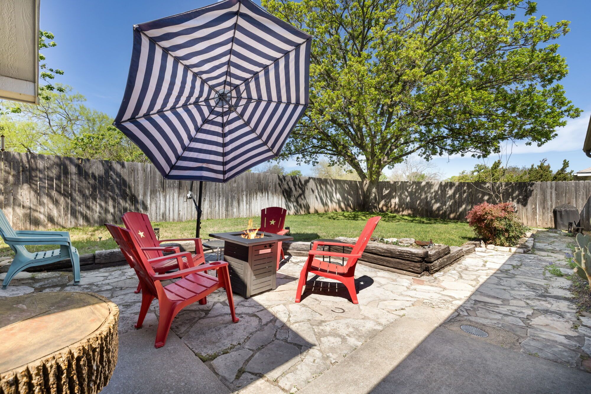 Eine Terrasse mit roten Stühlen, einem gestreiften Sonnenschirm und einer Feuerstelle.