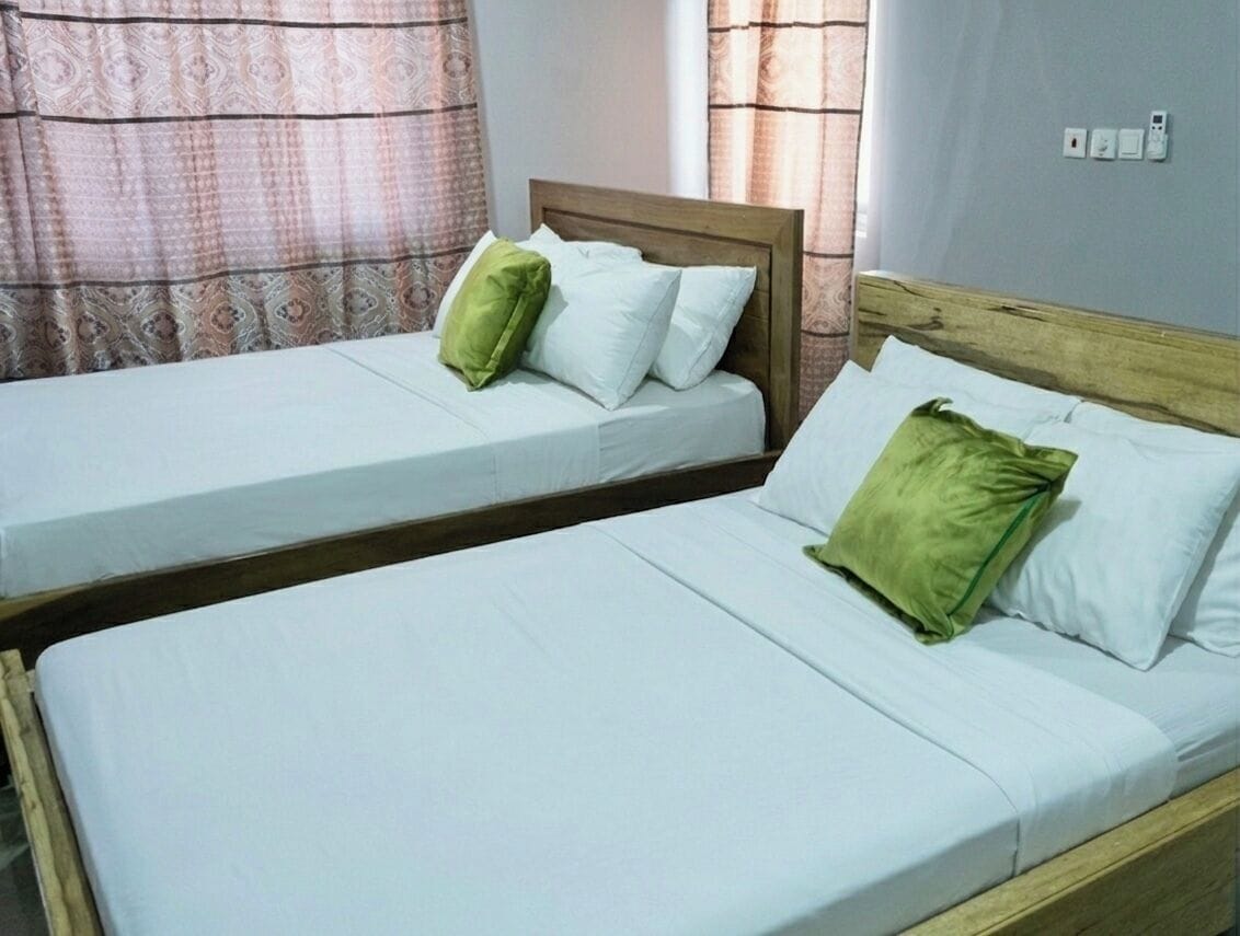 Two single beds with wooden frames, white bedding, and green pillows.