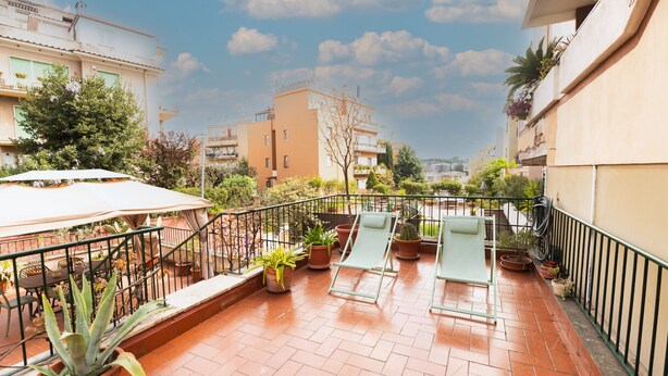 Terraço com plantas em vasos, uma mesa e duas cadeiras de descanso.