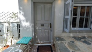A white door with a nameplate, a stone bench, and a stone-paved entrance. - Hydra studio with patio 250 meters up from port (Ydra)