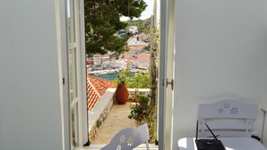 A room with a bed, a window, and a view of a harbor with boats and buildings. - Hydra studio with patio 250 meters up from port (Ydra)