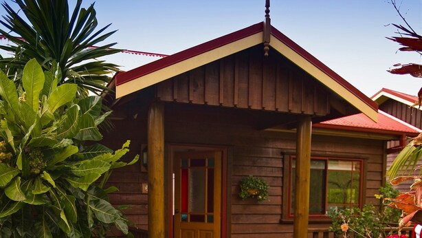 A wooden house with a red roof, a front door, and a small porch. - Jacaranda Park Holiday Cottages (Norfolk Island)