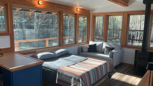 A bedroom with a bed, a sofa, a fireplace, and large windows. - Glamping tower north of Columbia Falls views of Whitefish mountain and privacy. (Columbia Falls)