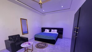 A bedroom with a bed, a chair, a small table, a mirror, and a ceiling fan.